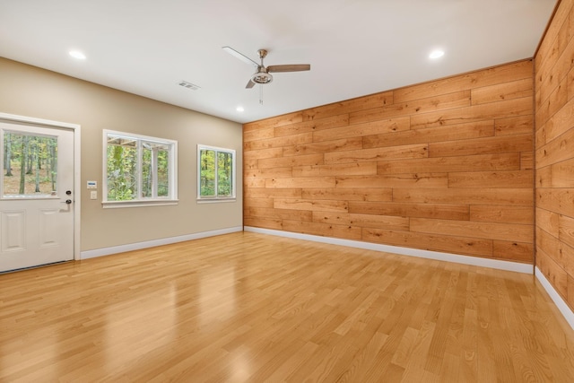 empty room with light wood-type flooring, a ceiling fan, visible vents, wooden walls, and baseboards