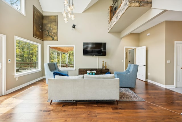 living area with wood-type flooring, baseboards, a high ceiling, and a notable chandelier