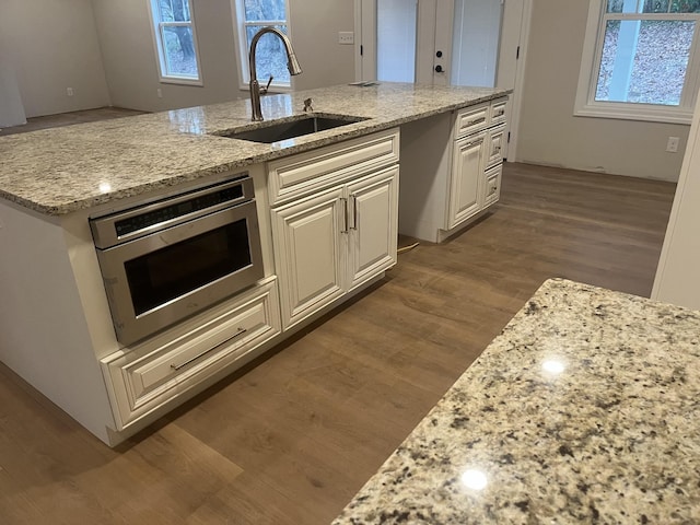 1168 N Franklin Ave, Cookeville, TN 38501 - kitchen featuring a sink, wood finished floors, light stone countertops, stainless steel microwave, and an island with sink
