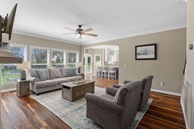 living room with baseboards, arched walkways, a ceiling fan, crown molding, and wood finished floors