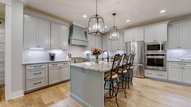 kitchen featuring custom exhaust hood, appliances with stainless steel finishes, a breakfast bar, light wood finished floors, and decorative backsplash