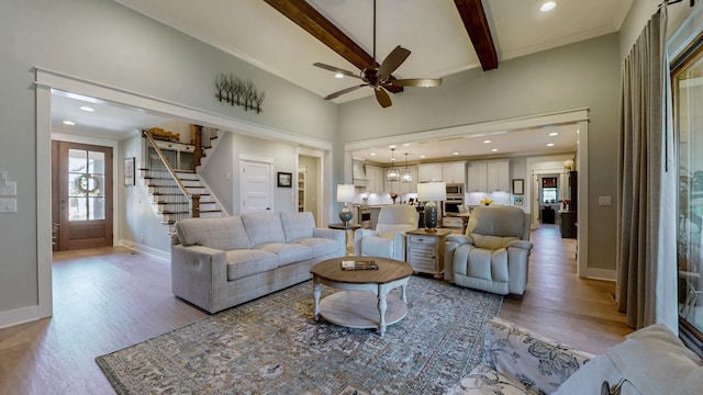 living area featuring stairs, light wood finished floors, beam ceiling, and ceiling fan