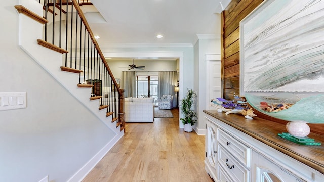 foyer featuring baseboards, crown molding, stairs, light wood-style floors, and ceiling fan