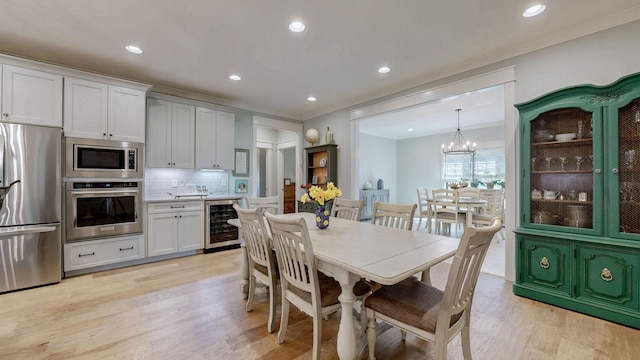 dining area with wine cooler, ornamental molding, light wood finished floors, and a notable chandelier
