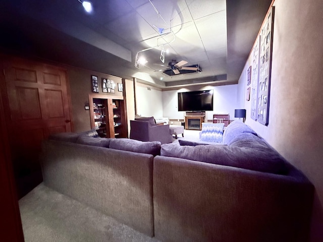 living room featuring a tray ceiling, ceiling fan, and a glass covered fireplace