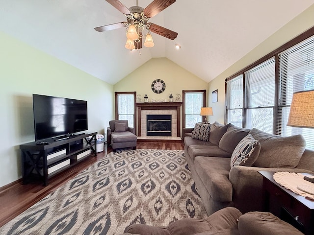 living room with a ceiling fan, vaulted ceiling, wood finished floors, a tile fireplace, and baseboards