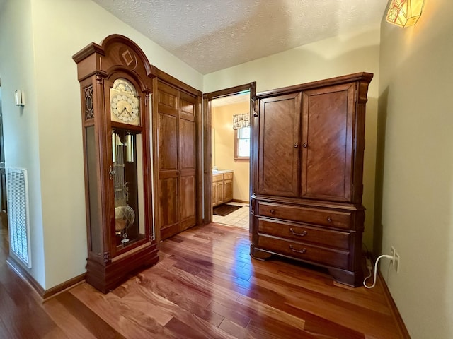 hallway with dark wood-type flooring, visible vents, baseboards, and a textured ceiling