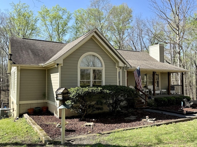 ranch-style house with cooling unit, a shingled roof, a chimney, and covered porch