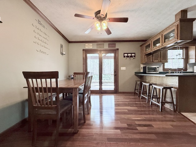 dining area featuring baseboards, ornamental molding, a textured ceiling, a ceiling fan, and dark wood-type flooring