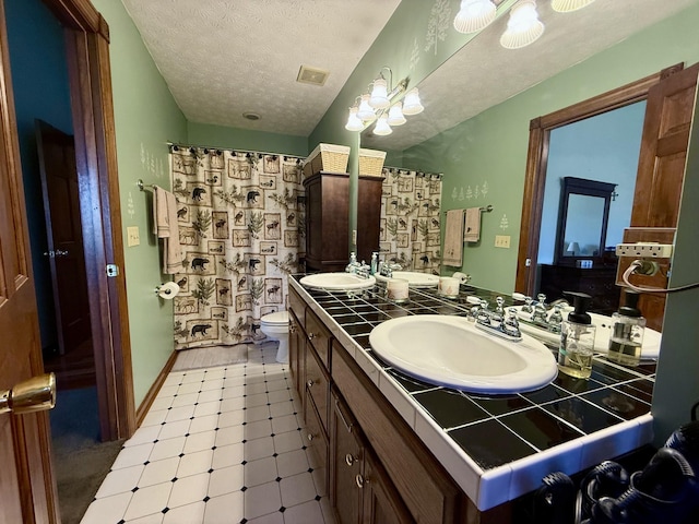 full bathroom with a sink, double vanity, curtained shower, and a textured ceiling