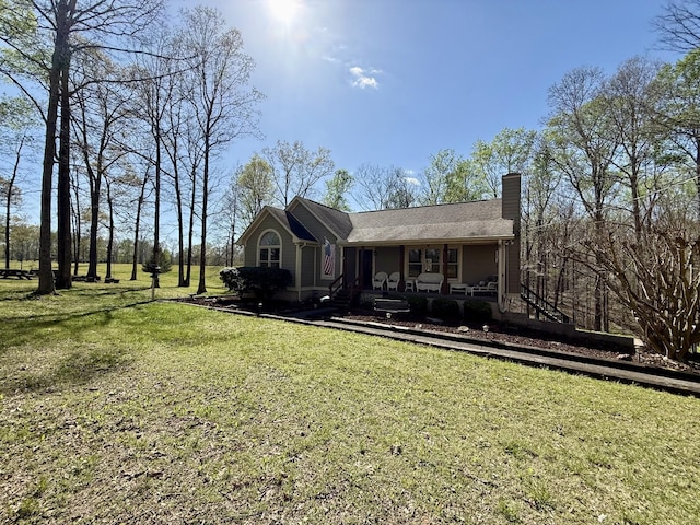 view of front of house featuring a chimney, covered porch, and a front yard