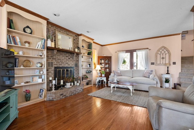 living room featuring crown molding, built in shelves, hardwood / wood-style floors, and a brick fireplace