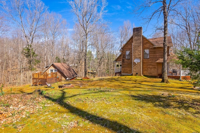 view of side of home featuring a deck, a yard, a fire pit, and a chimney