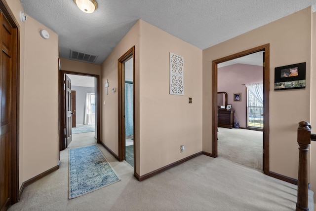hallway with baseboards, visible vents, light colored carpet, and a textured ceiling