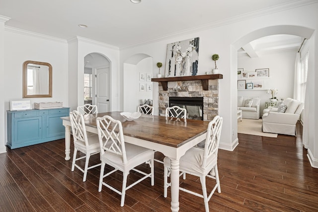 dining room with arched walkways, ornamental molding, dark wood-style floors, and a stone fireplace