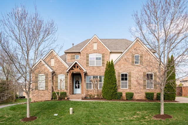 traditional home featuring brick siding, a front yard, and roof with shingles