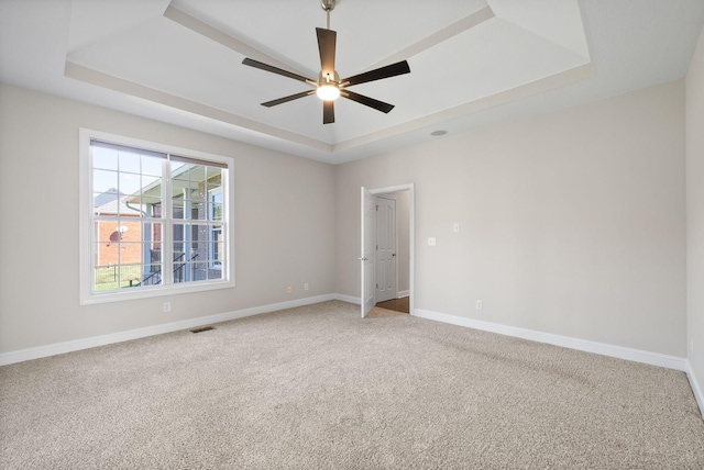 empty room featuring baseboards, light carpet, a ceiling fan, visible vents, and a raised ceiling