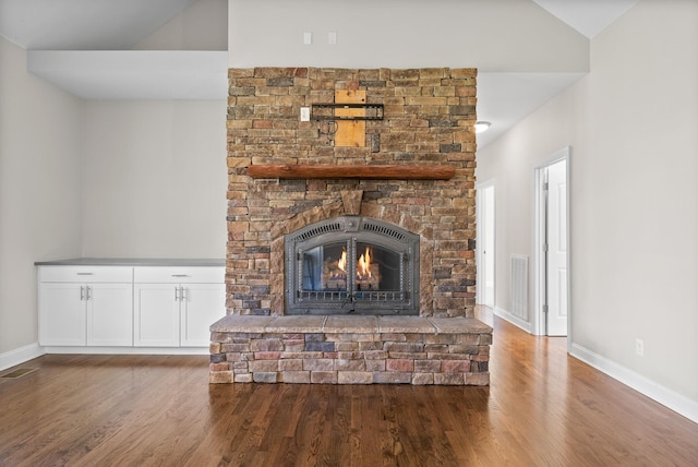 unfurnished living room with baseboards, wood finished floors, a fireplace, and visible vents