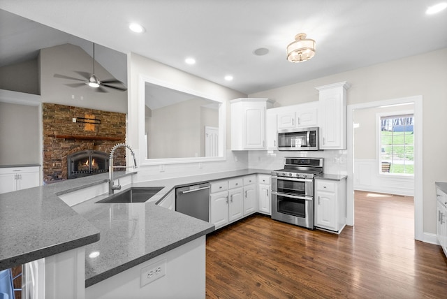 kitchen with ceiling fan, a fireplace, white cabinets, a sink, and stainless steel appliances