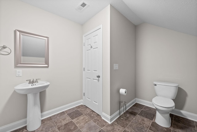 bathroom featuring visible vents, baseboards, toilet, stone finish floor, and a textured ceiling