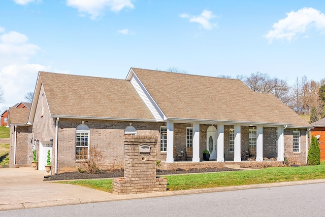 view of front of home featuring a porch, roof with shingles, concrete driveway, and brick siding