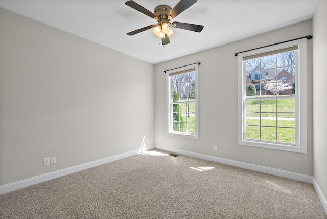 empty room with carpet flooring, baseboards, a ceiling fan, and visible vents
