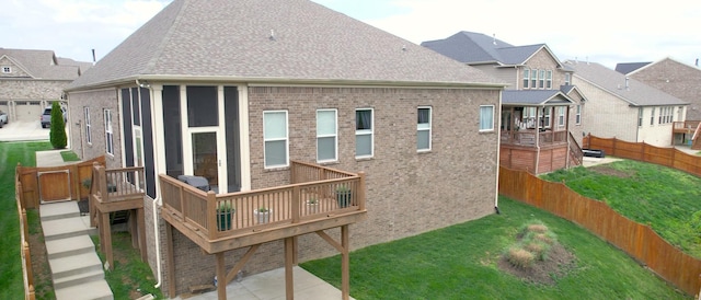 rear view of house with a shingled roof, a deck, a lawn, a fenced backyard, and brick siding