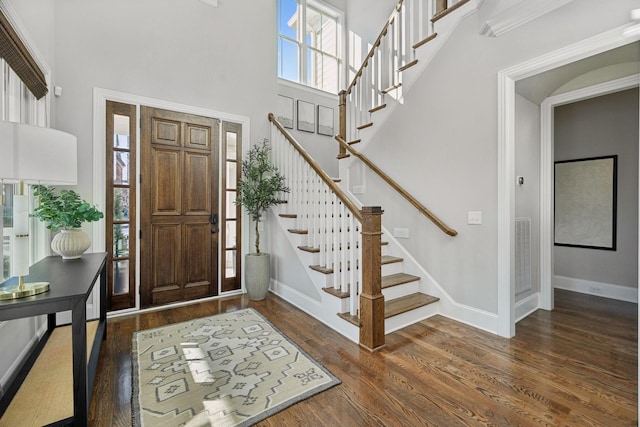 foyer entrance with wood finished floors, a towering ceiling, baseboards, and stairway