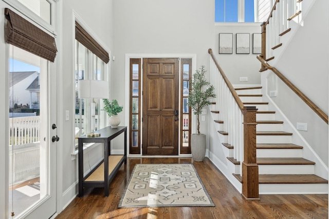 entrance foyer featuring stairway, a towering ceiling, baseboards, and wood finished floors