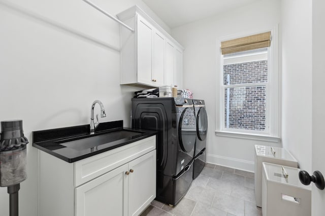 clothes washing area featuring a sink, washing machine and clothes dryer, cabinet space, and baseboards