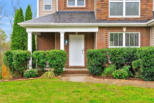 doorway to property featuring a yard, a shingled roof, and brick siding