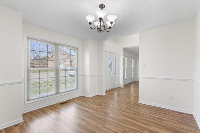 unfurnished dining area featuring a textured ceiling, visible vents, a chandelier, wood finished floors, and baseboards