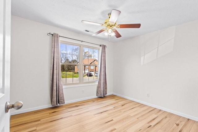spare room featuring wood finished floors, baseboards, a ceiling fan, and visible vents
