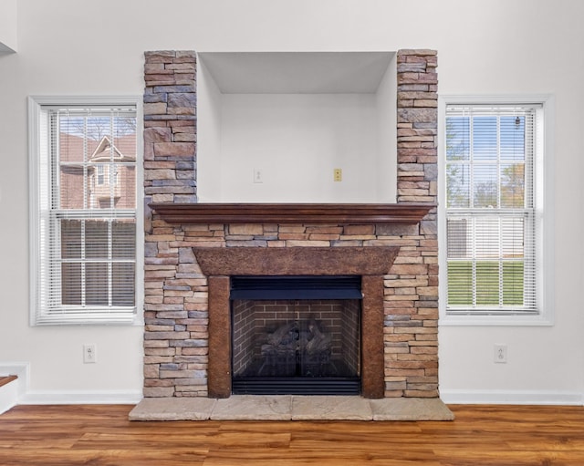 room details featuring a stone fireplace, baseboards, and wood finished floors