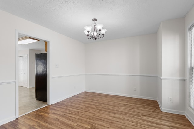 unfurnished room featuring a chandelier, a textured ceiling, wood finished floors, and baseboards