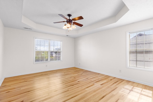 spare room with visible vents, baseboards, a raised ceiling, and light wood finished floors