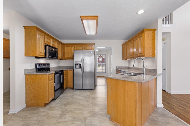 kitchen with a peninsula, light stone counters, a sink, stainless steel appliances, and baseboards