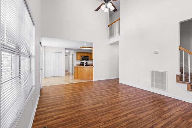 unfurnished living room with wood finished floors, baseboards, visible vents, and stairway