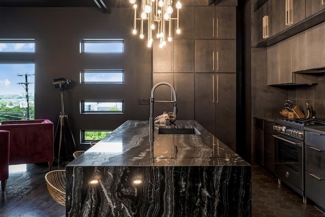 kitchen featuring a sink, dark stone counters, stainless steel stove, modern cabinets, and an island with sink