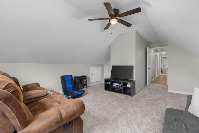 carpeted living area featuring baseboards, a wood stove, ceiling fan, attic access, and vaulted ceiling