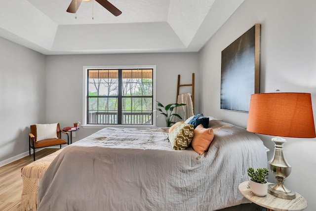 bedroom featuring a tray ceiling, wood finished floors, ceiling fan, and baseboards
