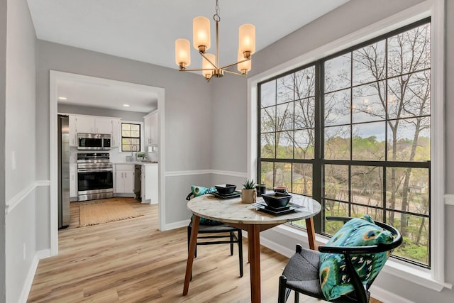 dining room with light wood-type flooring, a notable chandelier, and baseboards