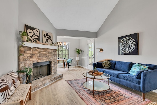 living area featuring high vaulted ceiling, an inviting chandelier, wood finished floors, a brick fireplace, and baseboards