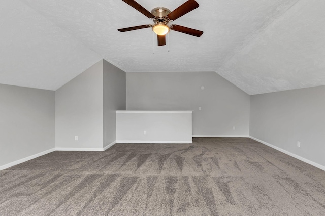 additional living space with a textured ceiling, dark colored carpet, a ceiling fan, and vaulted ceiling