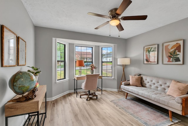 office area featuring light wood-style floors, baseboards, a ceiling fan, and a textured ceiling