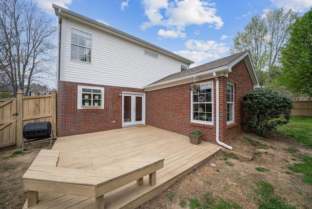 rear view of house with brick siding, french doors, fence, and a deck