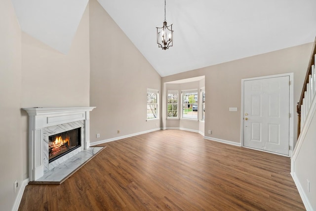 unfurnished living room featuring baseboards, wood finished floors, stairs, high vaulted ceiling, and a high end fireplace