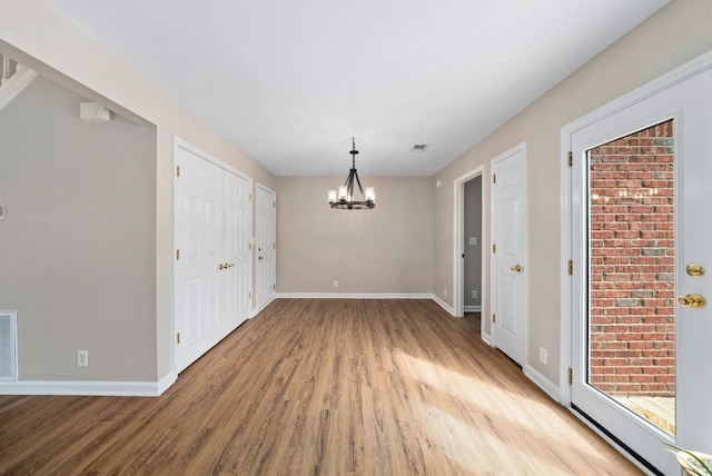 unfurnished dining area with visible vents, baseboards, an inviting chandelier, and wood finished floors