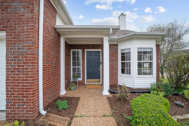 doorway to property with a garage, brick siding, and a chimney
