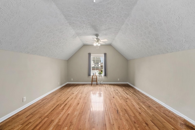 additional living space with light wood-type flooring, a textured ceiling, and baseboards